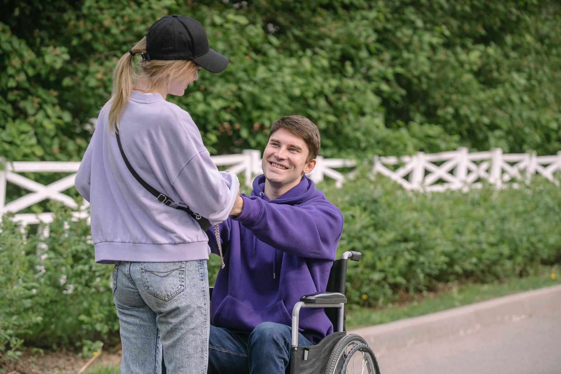 A man in a wheelchair chats and smiles with someone preparing fresh fruit and vegetables together in a bright home kitchen.